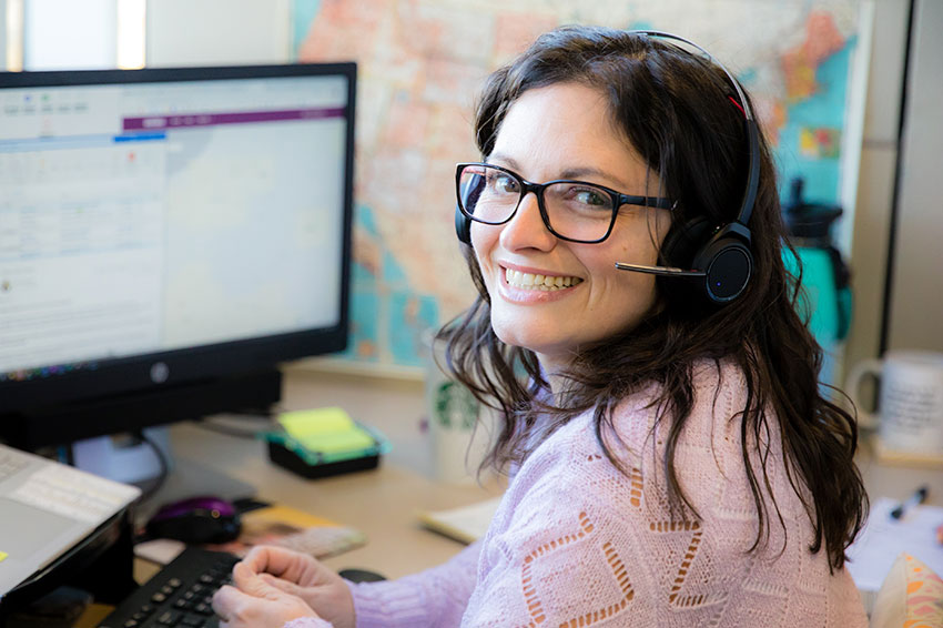 Home Instead support representative smiling while sitting at desk and wearing a headset
